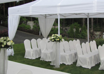 Krzesła okryte białymi pokrowcami pod białym namiotem na trawie - ślub w plenerze-